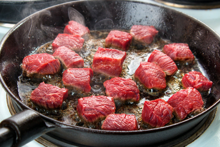 grass fed meat cooking in a black cast iron skillet on a stove