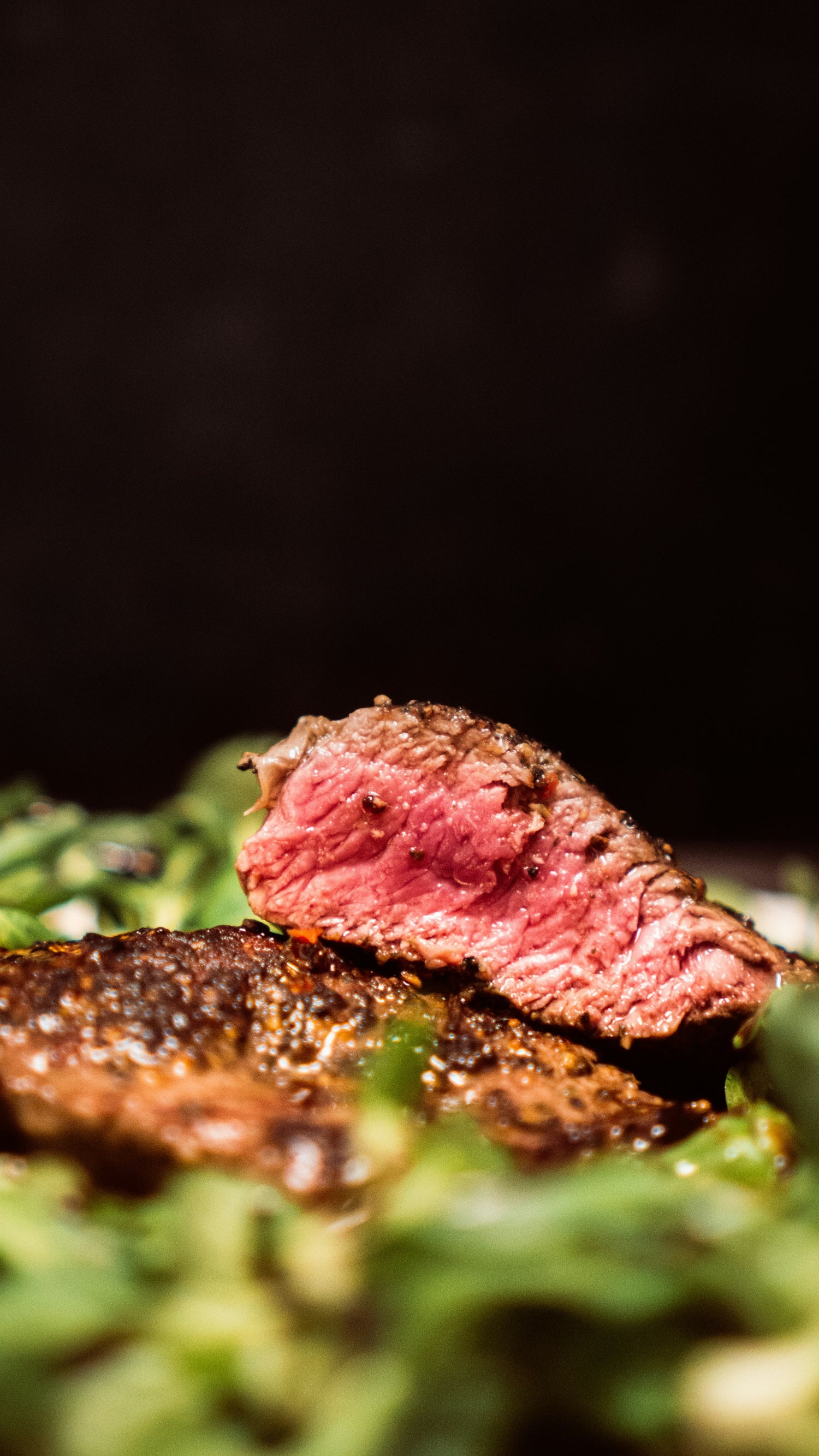 Close-up of a sliced piece of beef on a bed of greens with a dark background